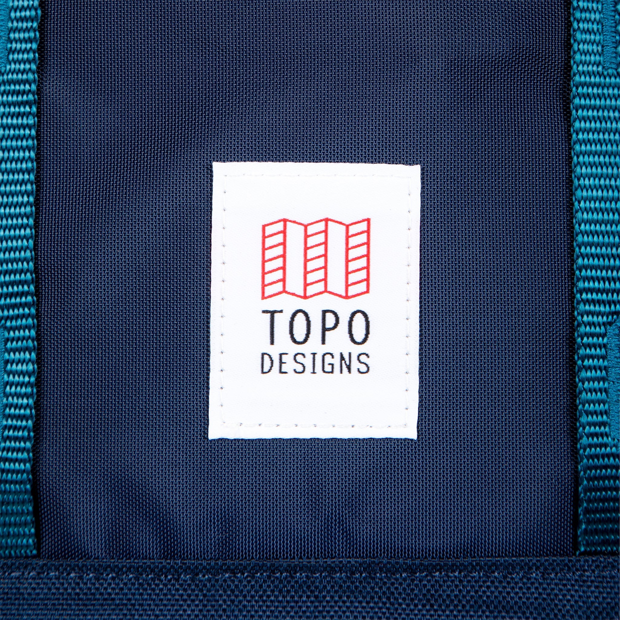 Topo Designs Global Travel Bag 30L Durable Carry On Convertible Laptop Travel Backpack in Navy blue showing close-up of front logo patch