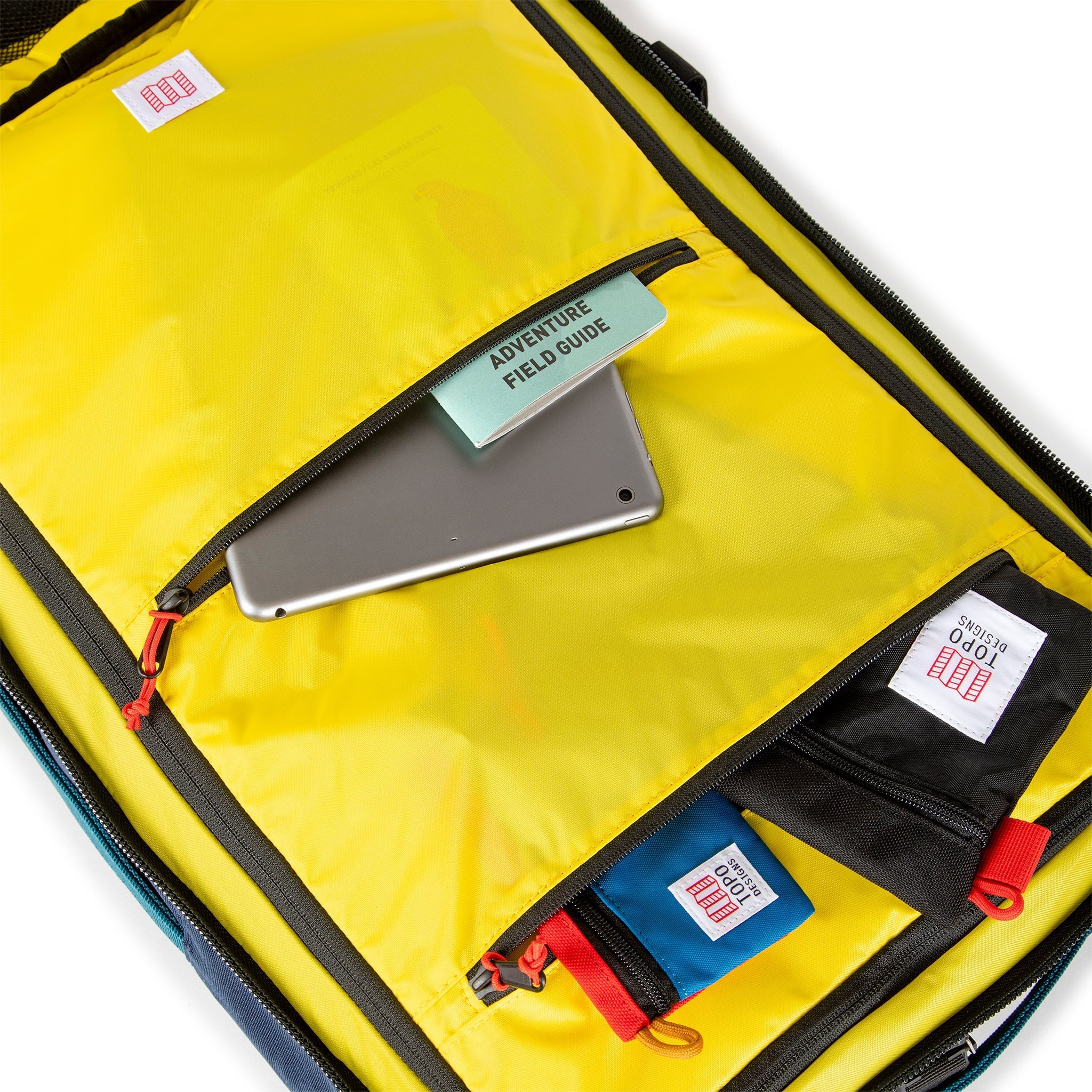 Yellow interior zipper pockets of Topo Designs Global Travel Bag 40L Durable Carry On Convertible Laptop Travel Backpack in Navy blue.