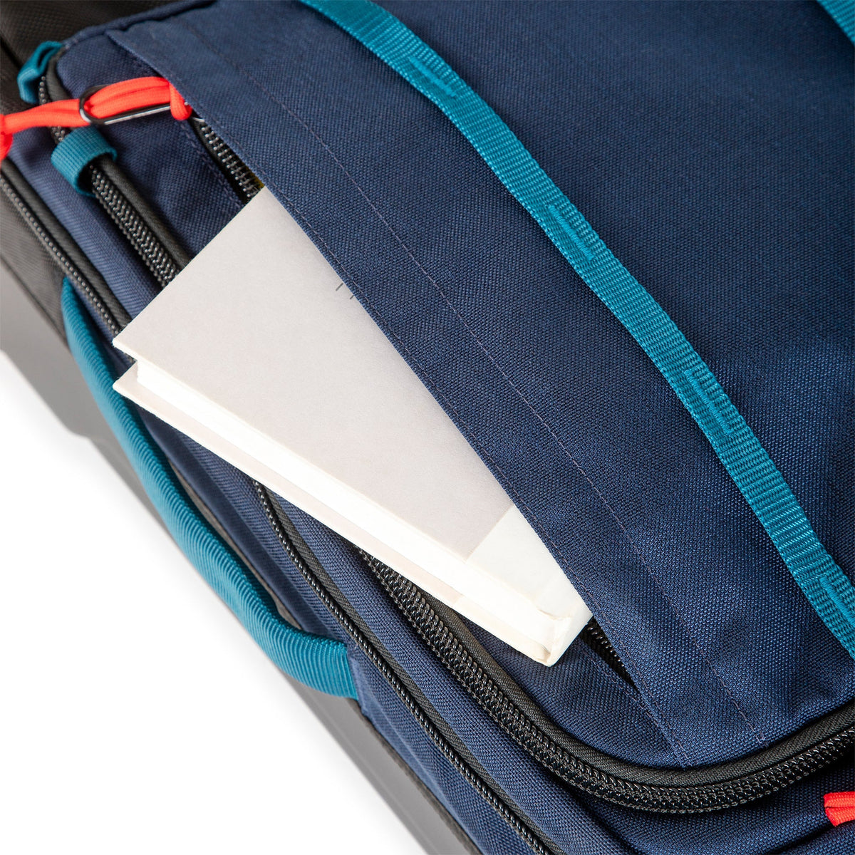 Front zipper pocket on Topo Designs Global Travel Bag Roller durable carry-on convertible laptop rolling backpack suitcase in Navy blue.