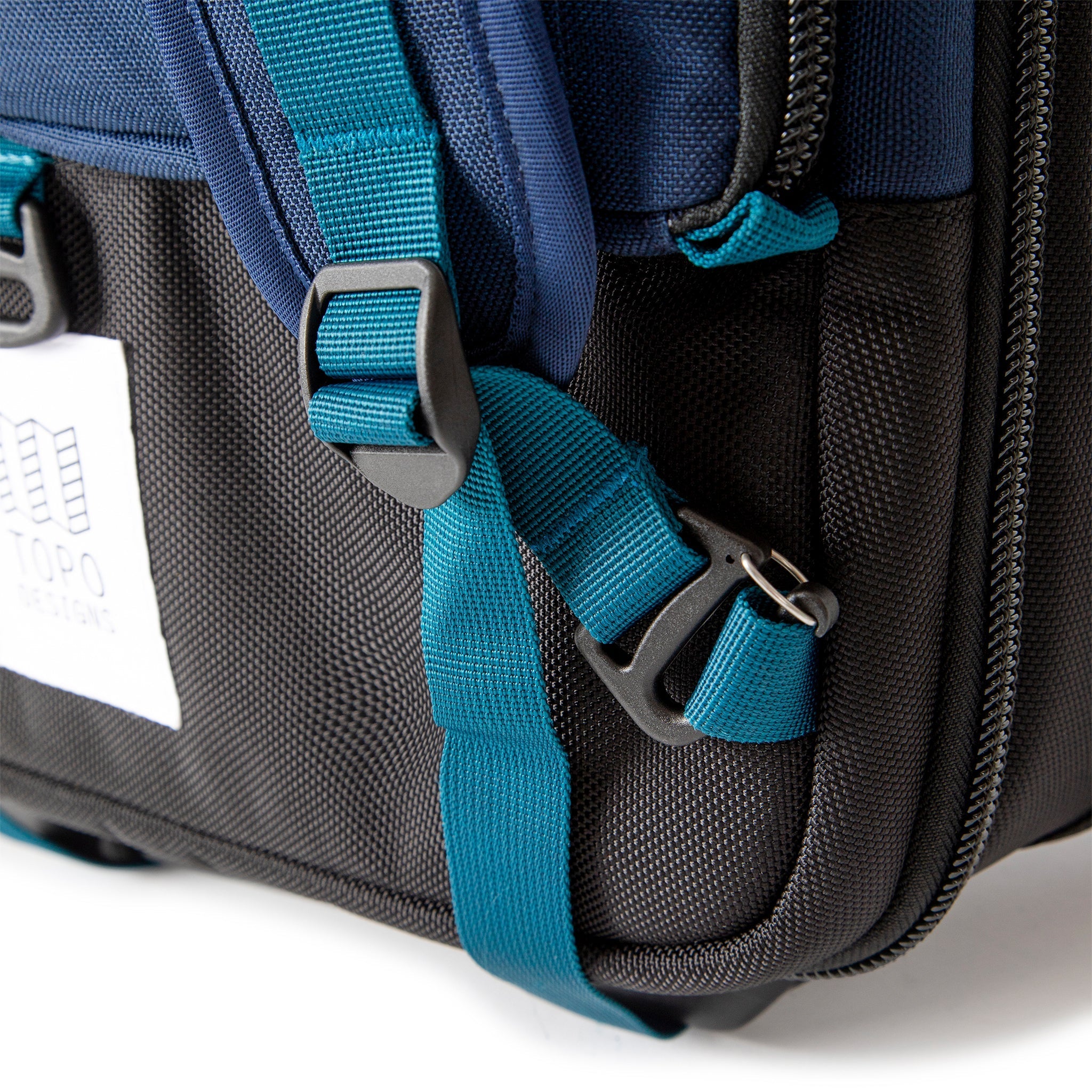 Backpack strap attachment points on Topo Designs Global Travel Bag Roller durable carry-on convertible laptop rolling suitcase in Navy blue.