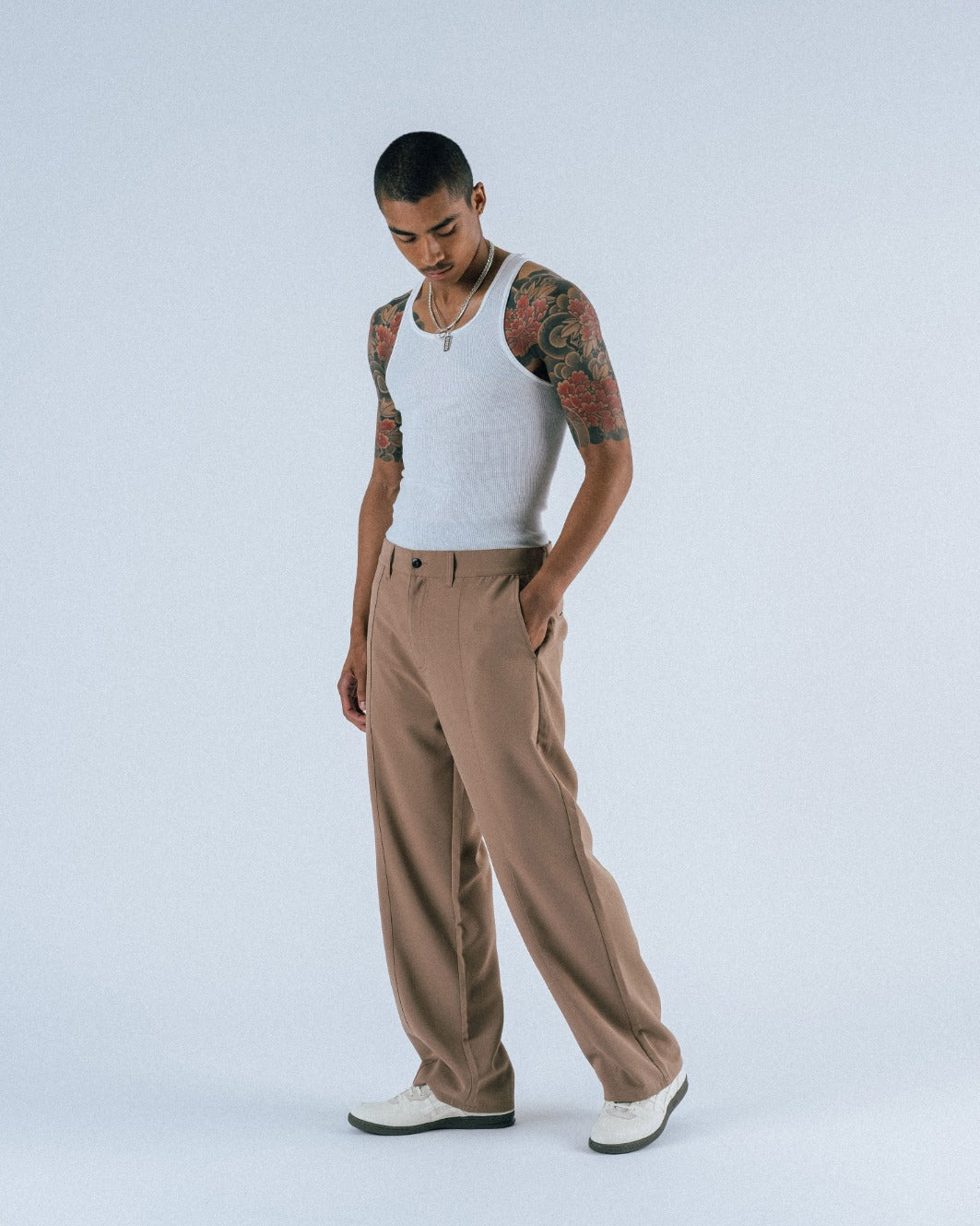 Person wearing a white tank top and brown pants on a light gray background