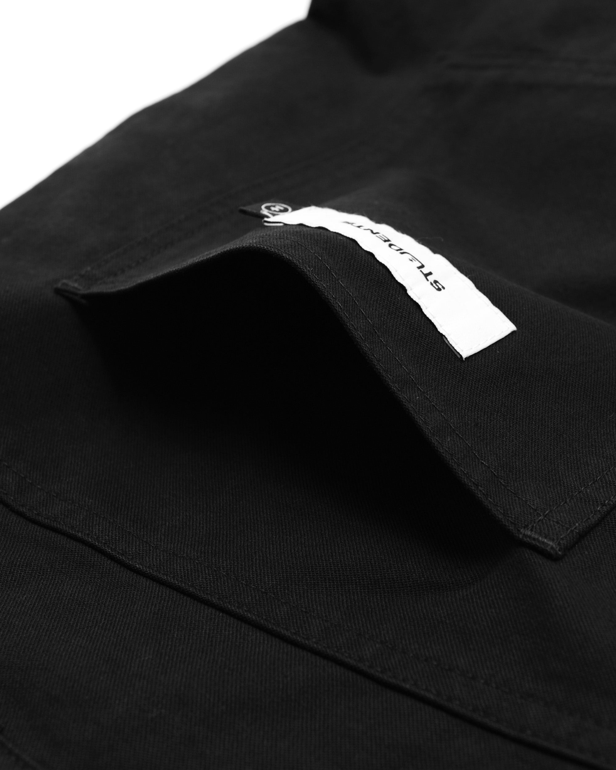 Close-up of a black pant
with a brand label on the chest pocket.