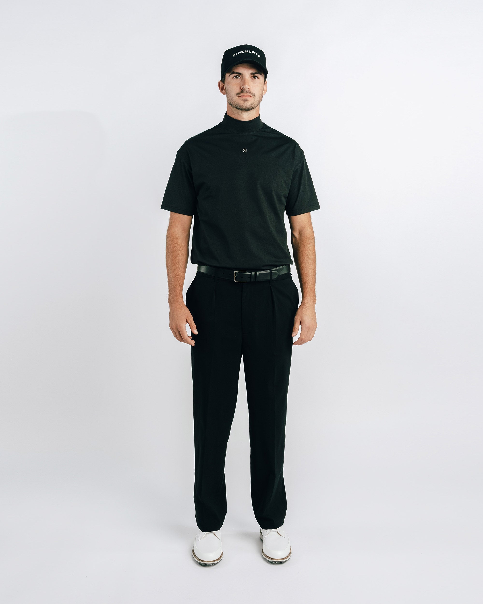 Man wearing a black polo shirt, black pants, and a black cap on a white background