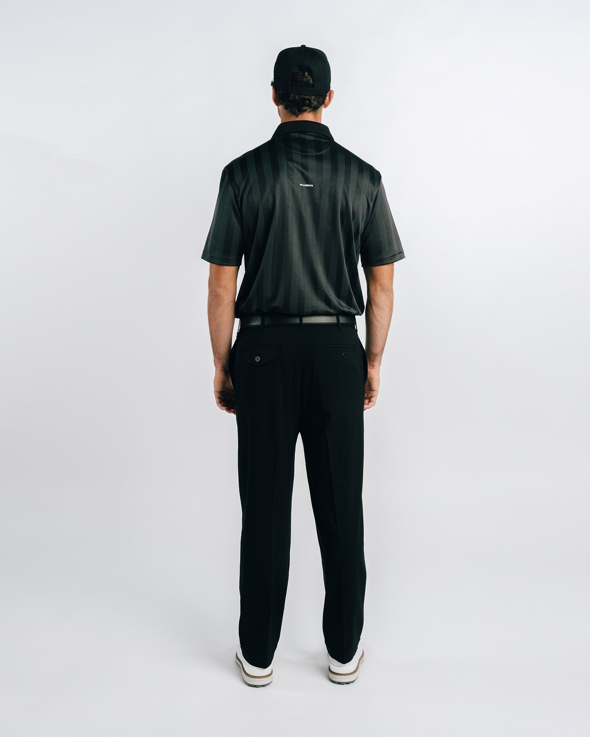 Person wearing a green polo shirt and black pants on a white background
