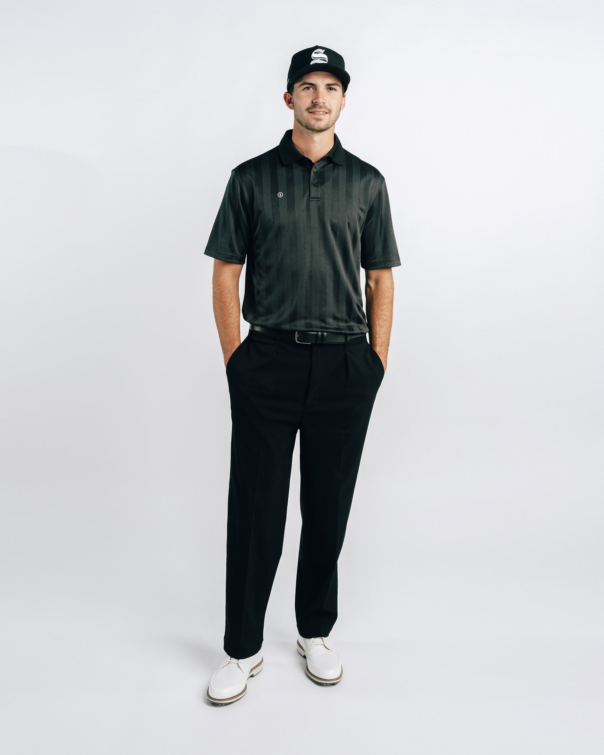 Man wearing a dark green polo shirt, black pants, and a cap on a white background
