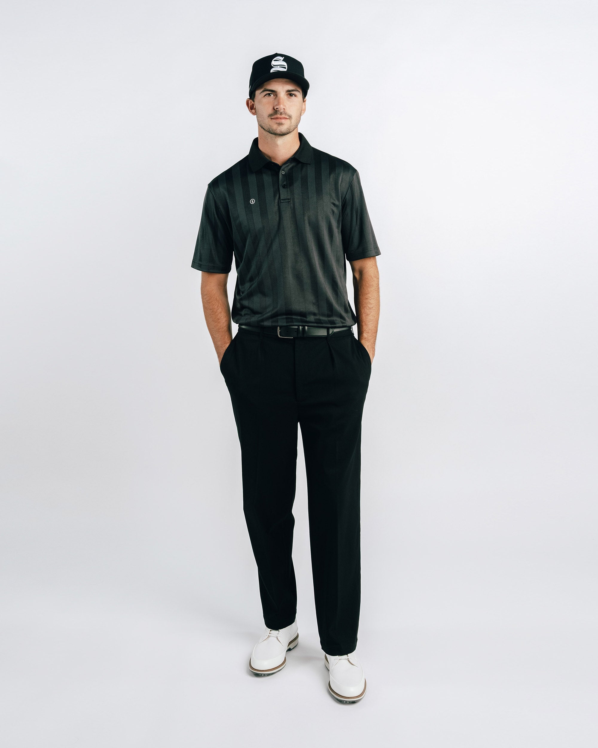Man wearing a dark green polo shirt, black pants, and a cap on a white background