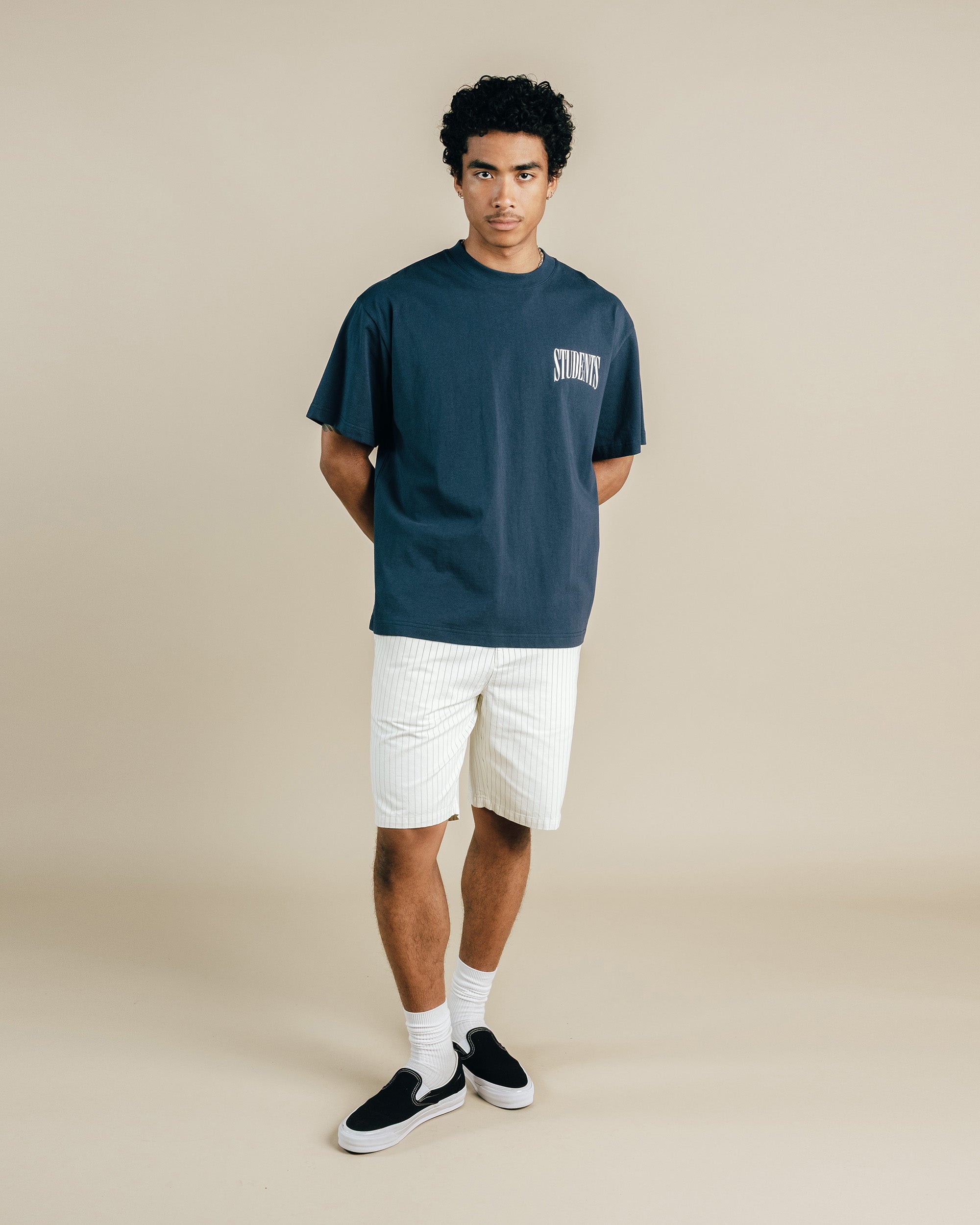Man wearing a dark blue t-shirt with 'Stonewall' text and white shorts on a beige background
