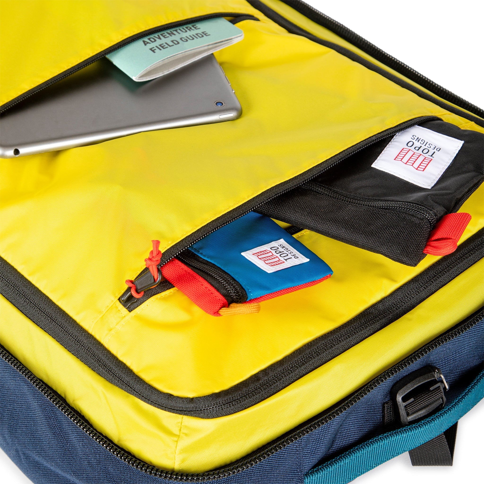 Yellow interior zipper pockets of Topo Designs Global Travel Bag 40L Durable Carry On Convertible Laptop Travel Backpack in Navy blue.