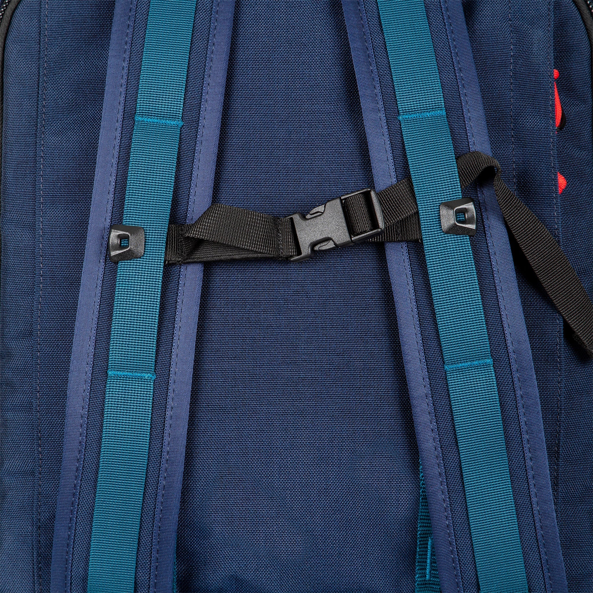 Sternum strap on backpack straps of Topo Designs Global Travel Bag Roller durable carry-on convertible laptop rolling suitcase in Navy blue.