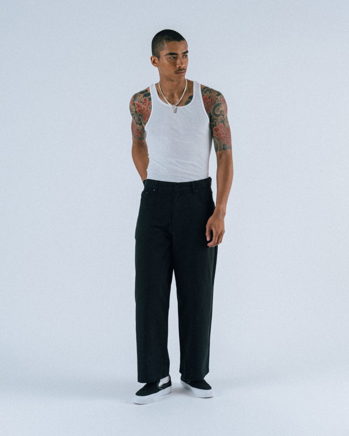 Man wearing a white tank top and black pants on a white background