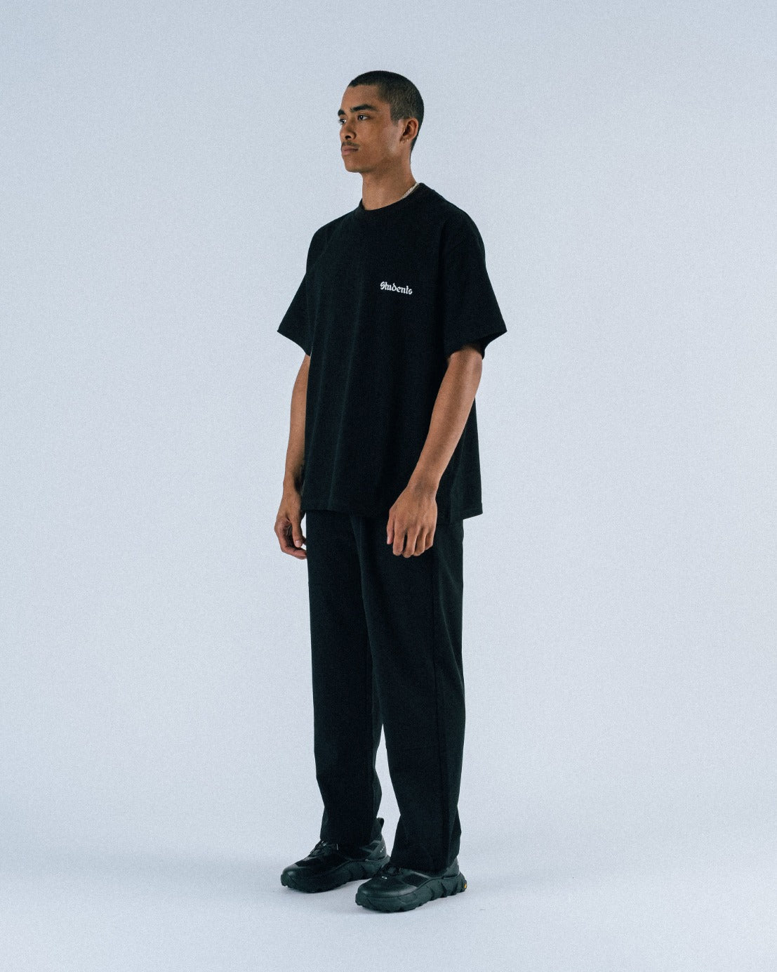 Person wearing a black t-shirt and pants with a brand logo on a white background