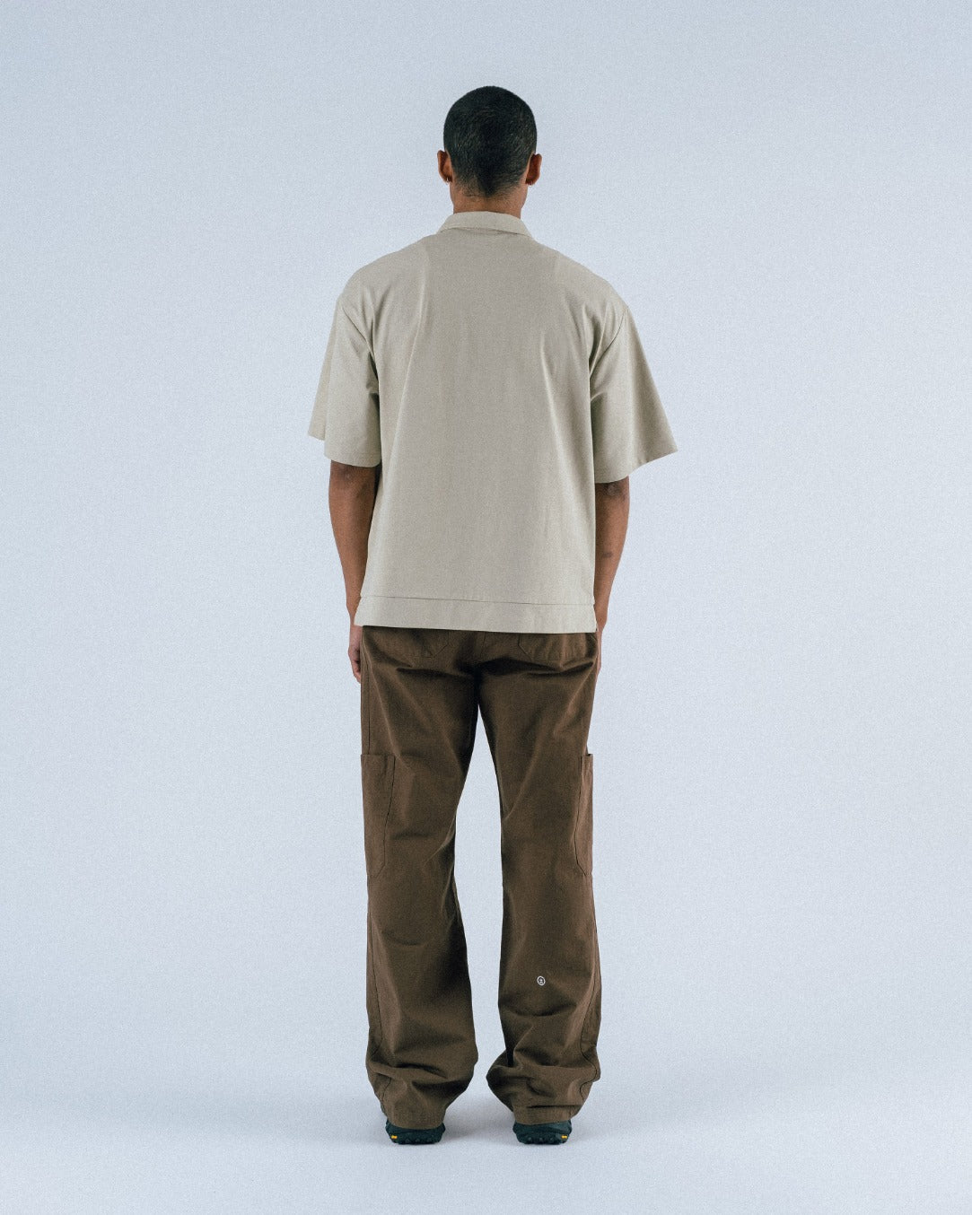 Person wearing a beige shirt and brown pants on a white background