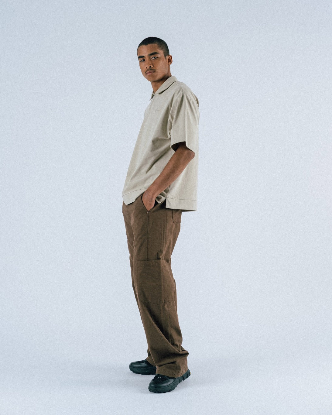 Man wearing a beige shirt and brown pants on a white background