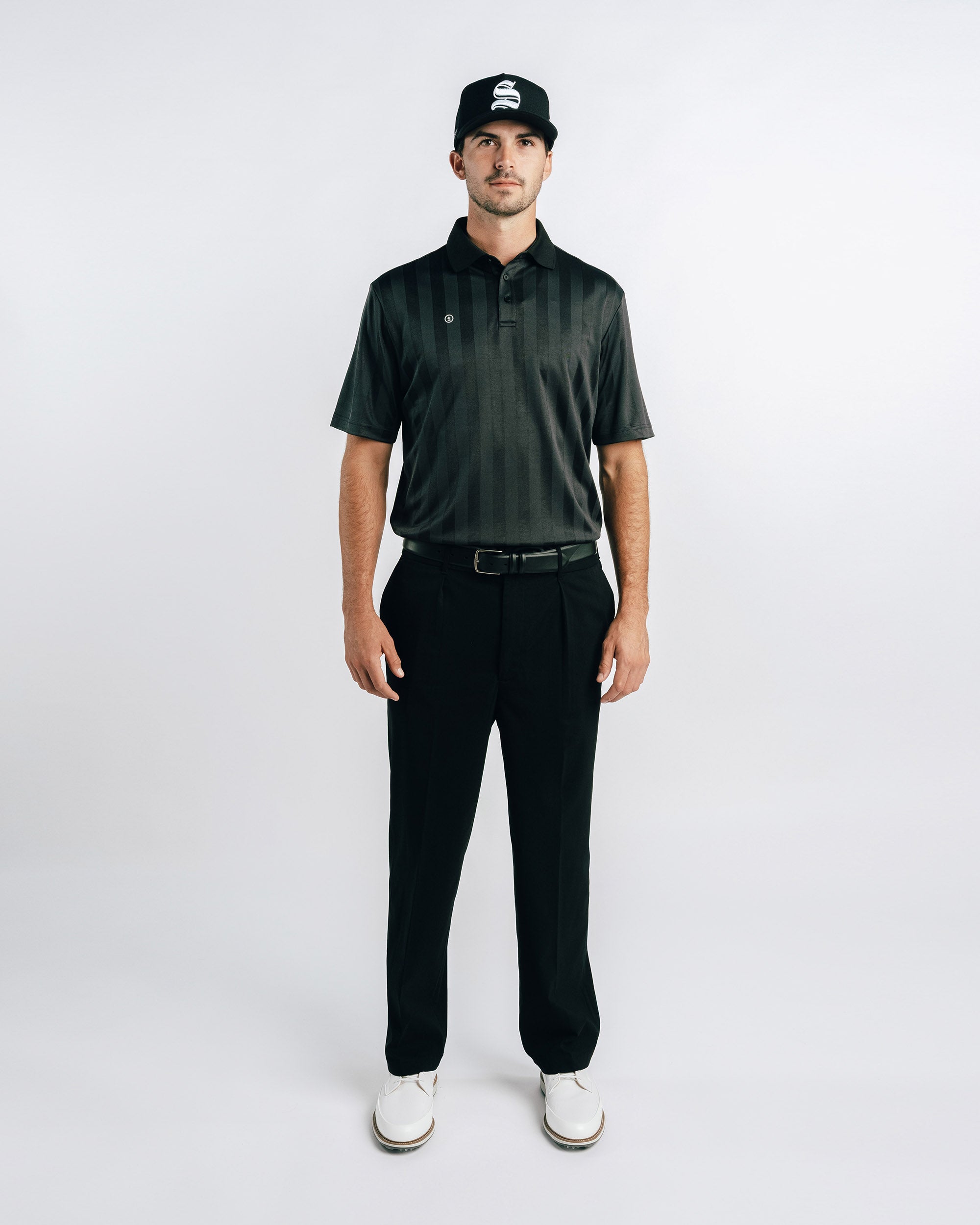 Man wearing a dark green polo shirt, black pants, and a black cap on a white background