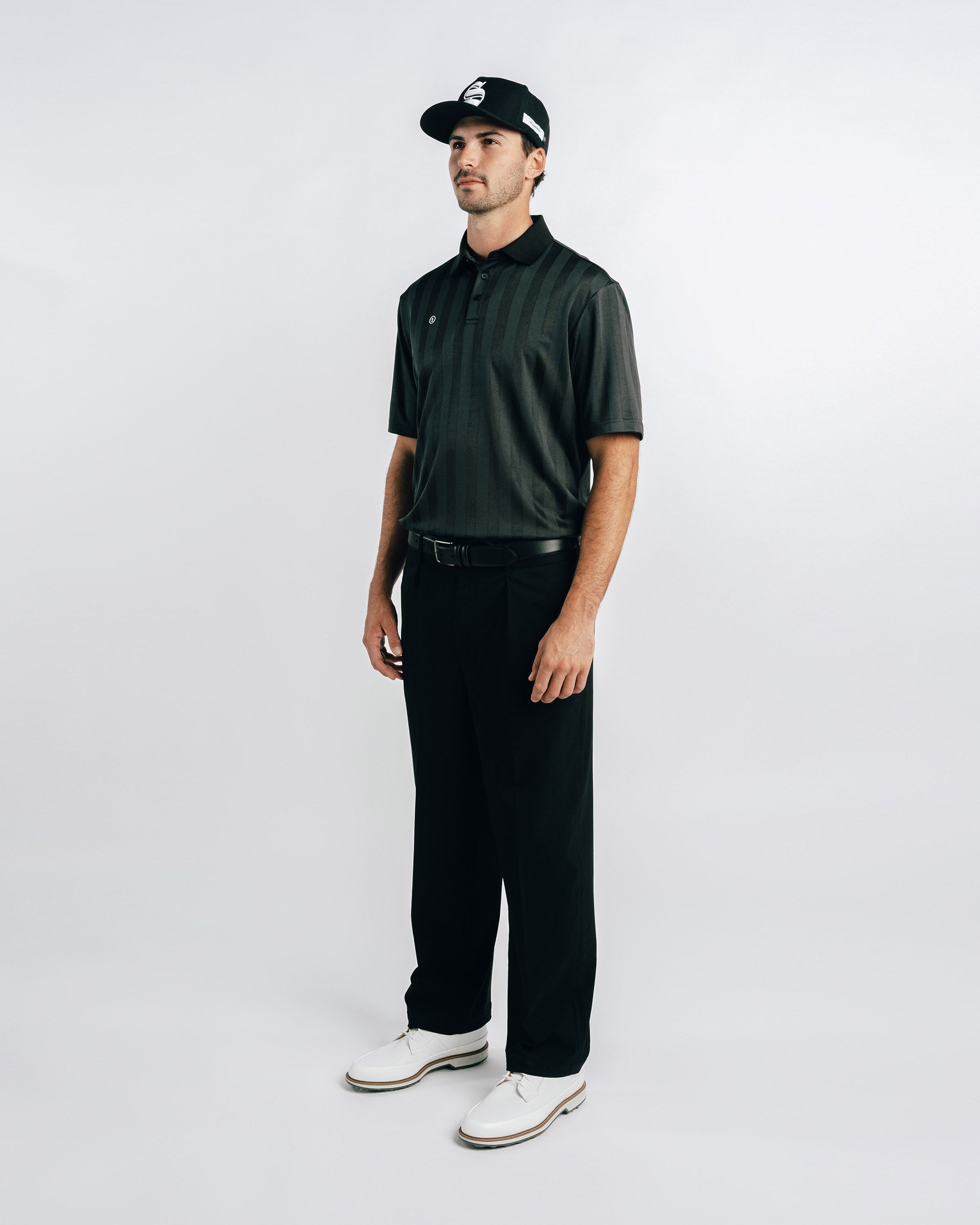 Man wearing a dark green polo shirt, black pants, and a cap on a white background