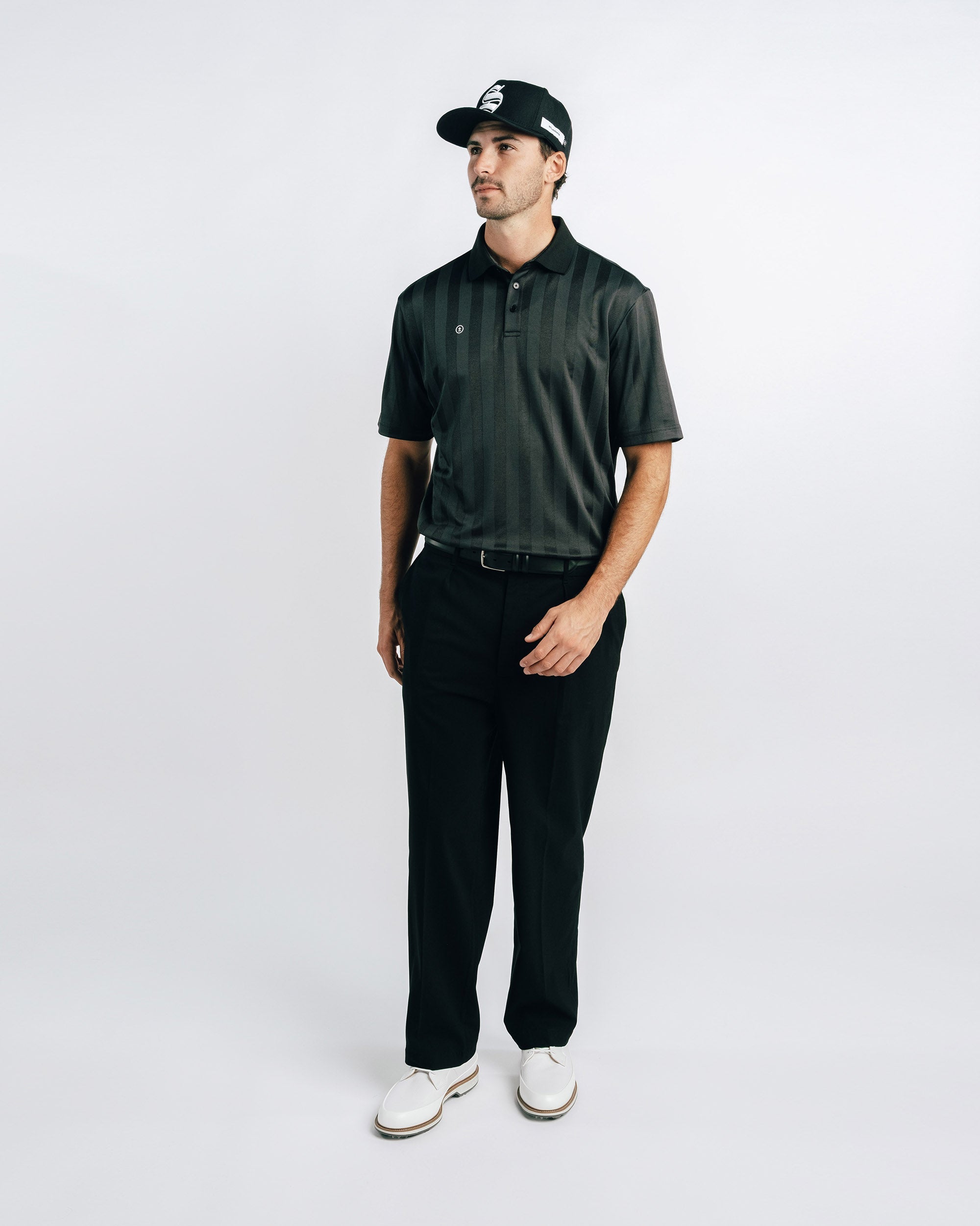 Man wearing a dark green polo shirt, black pants, and a cap on a white background