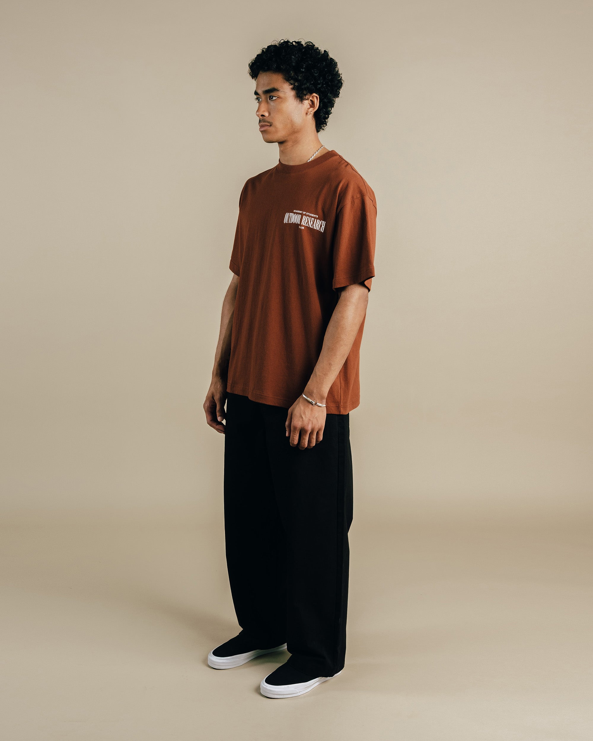 Person wearing a brown t-shirt and black pants on a beige background